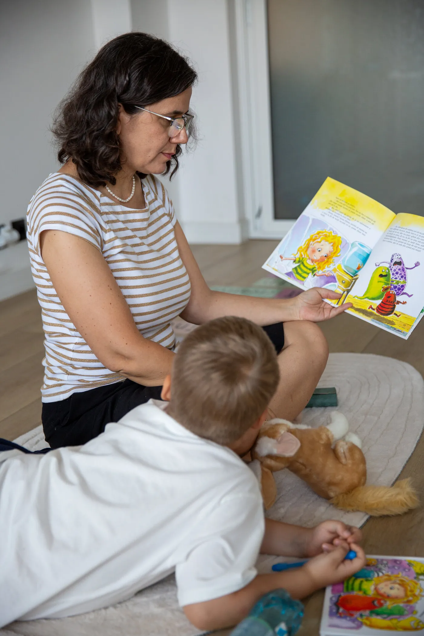Oana Hagiescu citind o carte ilustrată unui copil, așezați pe covor